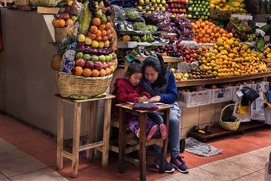  指导女儿家庭作业的水果摊老板，Steve McCurry摄于2017年厄瓜多尔。 