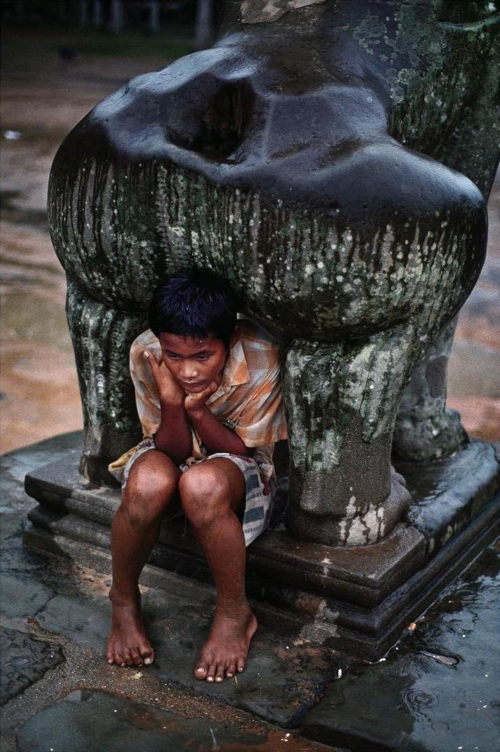  石像下躲雨的孩子，Steve McCurry摄于1999年柬埔寨吴哥窟。 