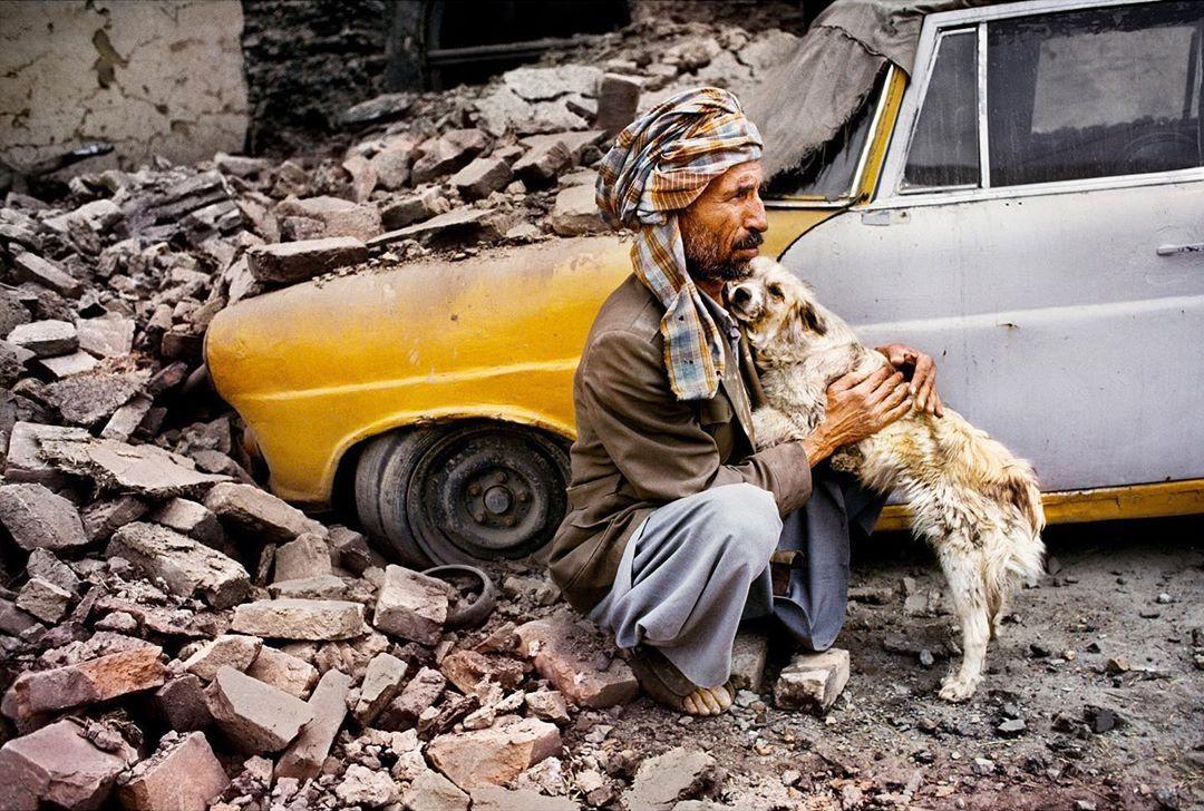  老人与狗，因为派系战争而导致建筑物坍塌毁坏了他的出租车，Steve McCurry摄于1992年阿富汗喀布尔。 